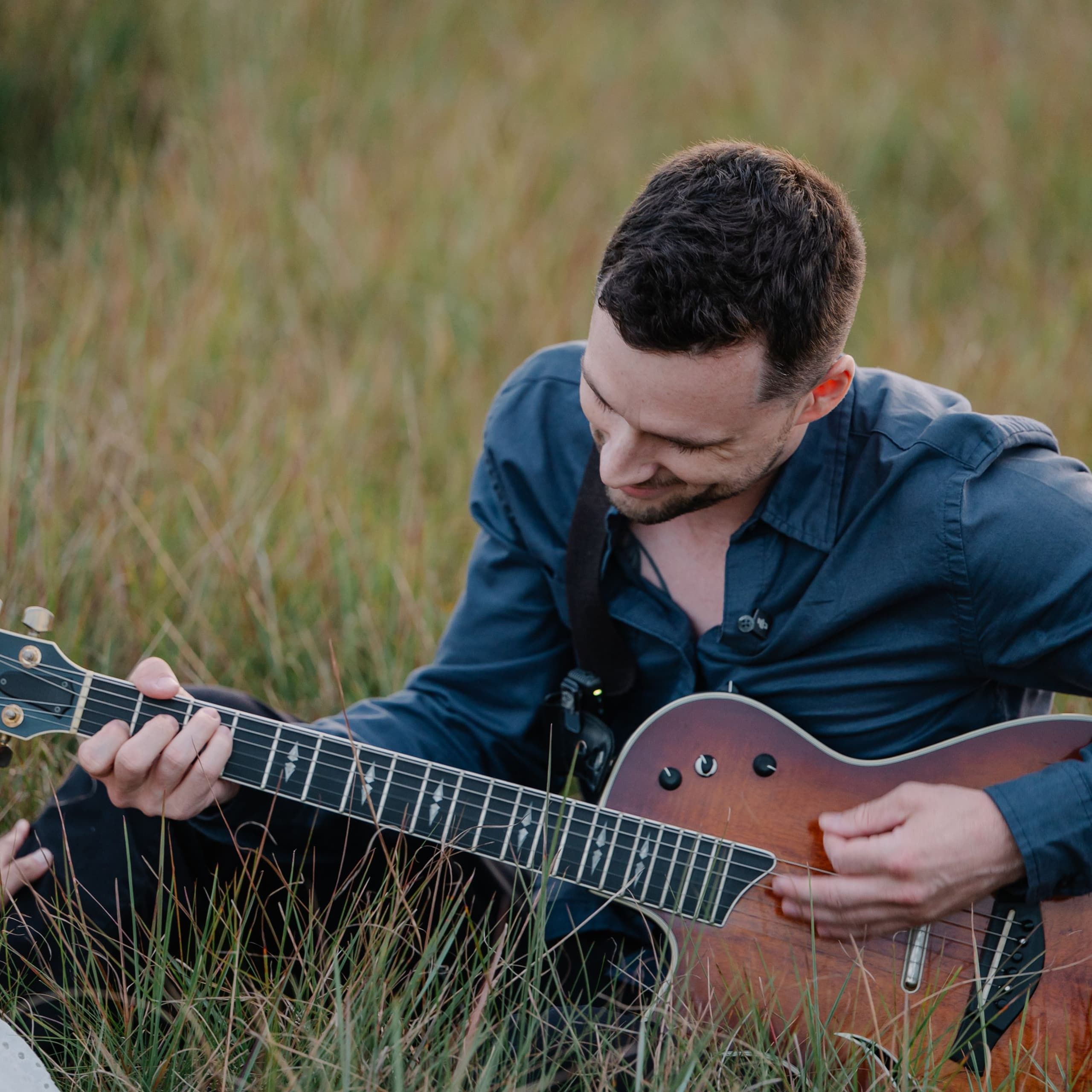 Noah Spott sitting in tall grass, playing guitar